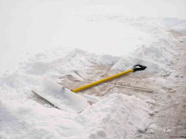 Ağır vasıflı sarı kar temizleyicisi beton bir yolda oturuyor. Etrafı taze beyaz kar yığınlarıyla çevrili..