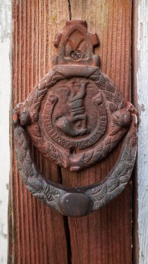Paslı, antika, dökme demir kapı tokmağının yakın çekimi. Süslü, kırmızı ahşap bir kapı..