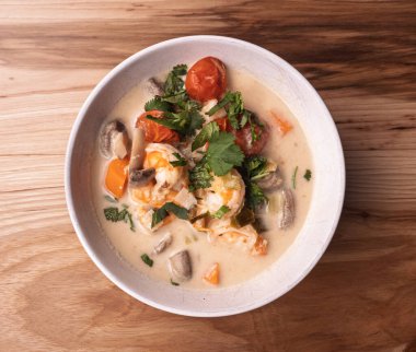 Tom Kha Goong 'un açık ahşap bir yüzeyde beyaz bir kasede yattığı, içinde büyük karides ve taze süslemeler bulunan temiz bir daire. Modern yemek blog biçimi.