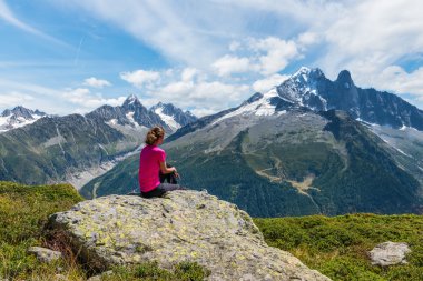 Girl sits on the stone and looks on the mountains in the sunny summer day