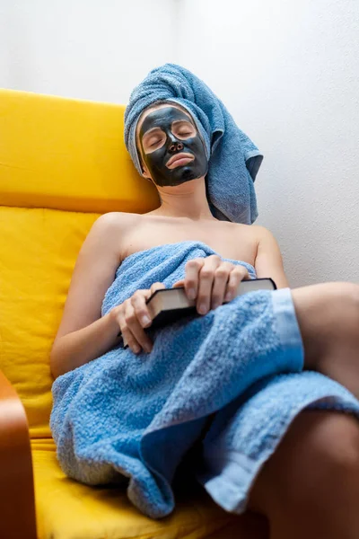 Young Woman Resting Couch Book Her Hands Black Facial Mask —  Fotos de Stock