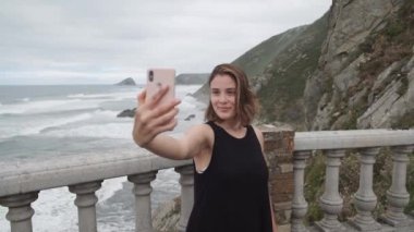 Kayalık bir sahilin önünde akıllı bir telefonla neşeli bir şekilde kendini kaydediyor..