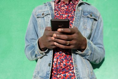 Afrikalı bir adamın yeşil arka planda akıllı telefon kullanmasının orta bölümü..