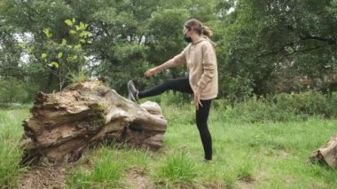 Yüzü maskeli bir kadın parkta bir kütüğe yaslanıyor..