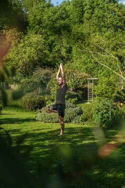 İspanyol adam bahçede yoga yapıyor. Ağaç duruşu yapıyor, Vrksasana. Dikey çekim.