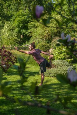İspanyol adam bahçede yoga yapıyor ve dansçı pozu veriyor, Natarajasana. Dikey çekim.