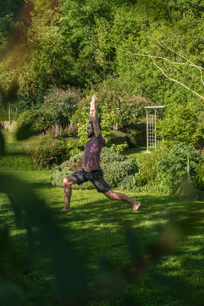 İspanyol adam bahçede yoga yapıyor. Savaşçı pozu veriyor, Virabhadrasana. Dikey çekim.