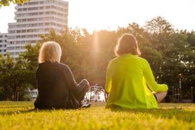 Büyükanne ve torun gün batımında parkta meditasyon yapıyorlar..