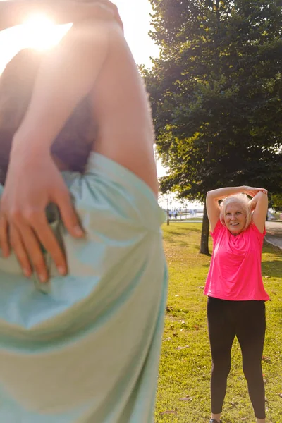 Parkta esneme hareketleri yapan sportif büyükanne ve torun. Dikey fotoğraf.