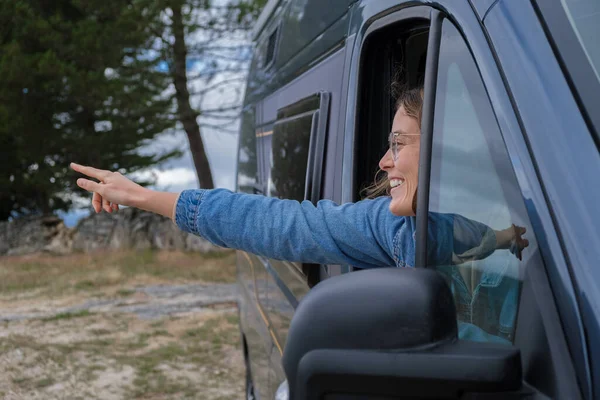Young woman pointing out the window of a camper van.