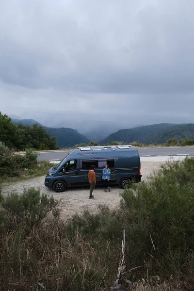 Young couple traveling in a van standing on the side of a road with beautiful views.