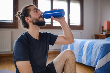 Sakallı bir adamın portresi. Su içiyor ve evde egzersiz yapıyor..