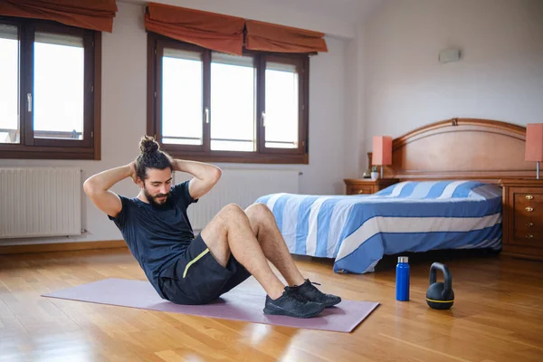 Sporty man with beard and bun hairstyle doing crunch while training at home.