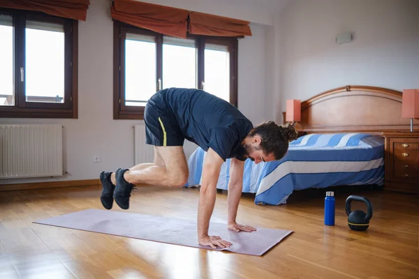 Man with beard and bun hairstyle doing mountain climber jump while training at home.