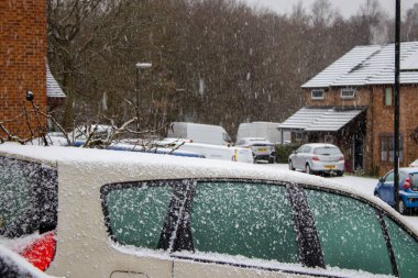 Arkasında bir sokak sahnesi olan bir arabanın üzerine kar yağıyor..