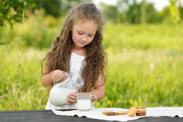 Linda niña vertiendo leche en vidrio desayunando verano al aire libre — Foto de Stock