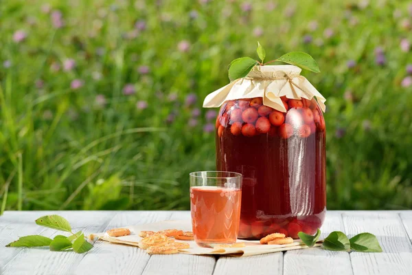 Домашний вишневый консервированный компот в стекле с печеньем на белом деревянном столе в саду — стоковое фото
