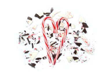 Beyaz arka planda ev yapımı naneli çikolata kabuğu kırıntıları olan kalp şeklinde iki kırmızı şeker kamışı. Düz tabaka, üst görünüm.