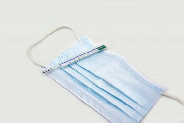  Mavi, tek kullanımlık koruyucu tıbbi yüz maskesi ve beyaz arka planda izole edilmiş termometre. düz yatış, üst görünüm.