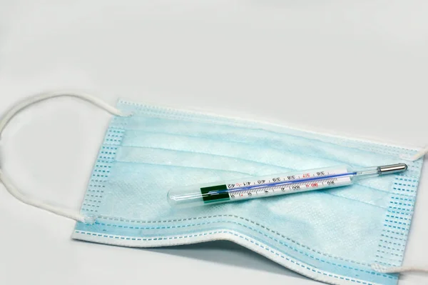 Blå engångs skyddande medicinsk ansiktsmask med termometer isolerad på vit bakgrund. platt låg, ovanifrån — Stockfoto