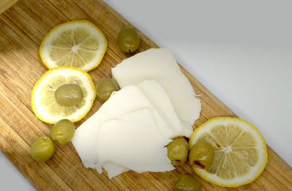 Сыры, лимон и оливки на деревянной доске. Подавать антипасто на старой светлой деревянной доске. — стоковое фото