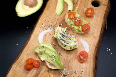  Tahta tahtada tohum ve domatesli avokado tostları, koyu arkaplan. Avokado sandviçlerinin üst görüntüsü. Yemek fotoğrafı, sağlıklı yiyecekler..