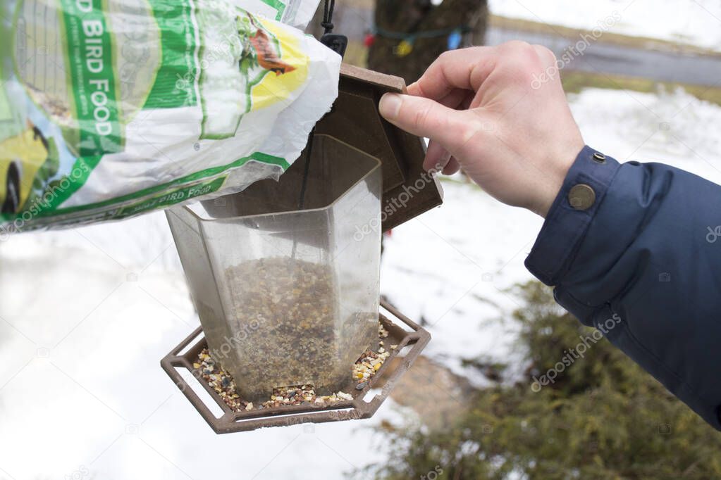 man refilling bird feeder with seeds during winter. Taking care of hungry birds.