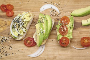 Kahvaltı için çeşitli sandviçler, tahtanın üzerinde tohum ve domatesli aperatifler, karanlık arka plan. Avokado sandviçlerinin üst görüntüsü. Yemek fotoğrafı, sağlıklı yiyecekler..