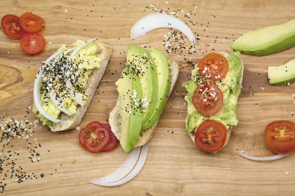 Kahvaltı için çeşitli sandviçler, tahtanın üzerinde tohum ve domatesli aperatifler, karanlık arka plan. Avokado sandviçlerinin üst görüntüsü. Yemek fotoğrafı, sağlıklı yiyecekler..