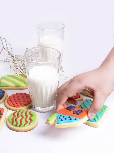 Vaso de leche y galletas de mano. Galletas coloridas colocadas junto a ella en la mesa sobre fondo blanco. — Foto de Stock