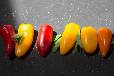 colorful mini peppers and mint leaves on black sunny background. Above view of yellow, red and orange peppers