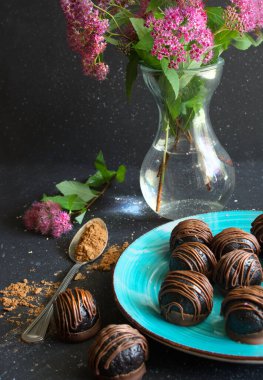Çikolatalı trüf ya da mavi tabakta şekerler, vazoda çiçekler koyu arkaplanda