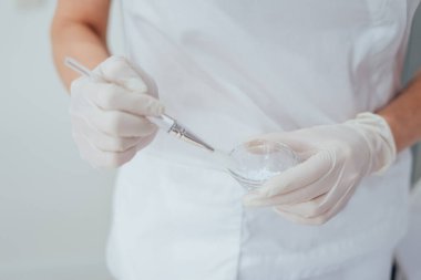 Güzellik salonunda beyaz eldivenli kozmetik uzmanı yüz maskesi takıyor plastik kasede cilt bakımı için hazırlanıyor.
