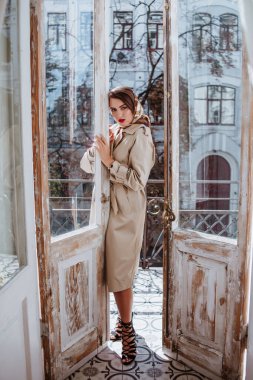 Genç ve güzel bir esmer balkonda poz veriyor. Şık bir trençkot giyen, ipek atkı takan bir kadın. Sonbahar mevsimi.