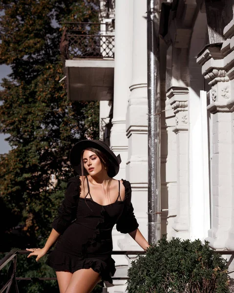 ブラックのミニドレスとサンハットを着た魅力的な女性 バルコニーでリラックスした女性 明るい白人女性の写真 — ストック写真