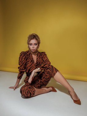 Genç sarışın kadın yerde oturuyor. Sarı arka planda poz veren manken. Glamour retro tarzı. Hayvan desenli giysiler