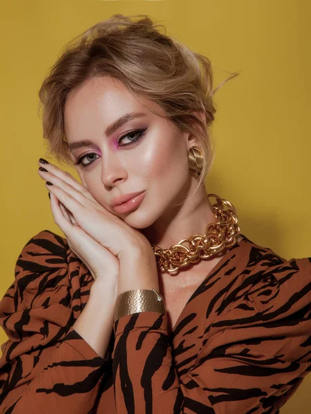 Retro style fashionable woman with vintage outfit on yellow background. Blonde woman wearing tiger print dress, massive gold jewelry. happy lady posing in studio. glamour woman with bright make-up and volume hairstyle. Close-up beauty.