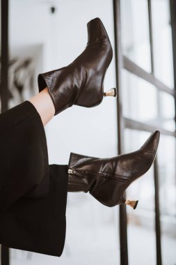 Siyah deri çizmeli, parlak bir arka planı olan bir kızın bacakları. Moda fotoğrafçılığı modaya uygun görünüm kitabı yeni ayakkabı koleksiyonu sonbahar kış mevsimi