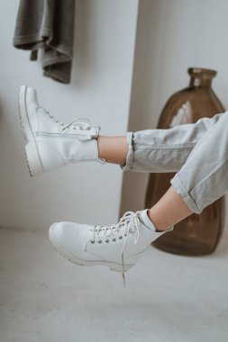 Bacaklarını kapalı mekanda poz veren şık bir kadının beyaz botlarıyla kapat. Modaya uygun deri çizmeli, kot pantolonlu hippi kız. Kadın Ayakkabısı