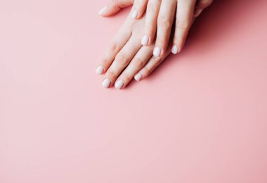 Profesyonel manikürlü, tırnakları beyaz renge boyanmış ve parlak bir ışıkla kaplı iki güzel kadının yakın görüntüsü. Tırnakların çıplak stil tasarımı. 