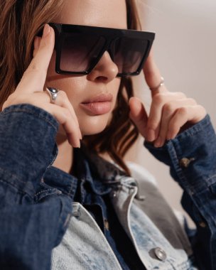Moda gözlükleri takan genç ve güzel bir kadın. Yakın çekim stüdyo portresi. Kısa kıvırcık saçlı bayan. Kot ceket giyen bir model. moda yakın plan portresi