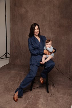 Mavi takım elbiseli ve küçük oğluyla poz veren bir kadın. Mutlu çocuğu olan güzel bir anne. 5 aylık erkek bebek.