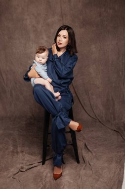 Mavi takım elbiseli ve küçük oğluyla poz veren bir kadın. Mutlu çocuğu olan güzel bir anne. 5 aylık erkek bebek.