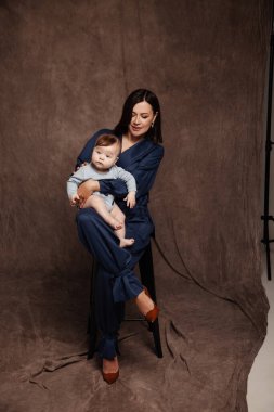 Mavi takım elbiseli ve küçük oğluyla poz veren bir kadın. Mutlu çocuğu olan güzel bir anne. 5 aylık erkek bebek.