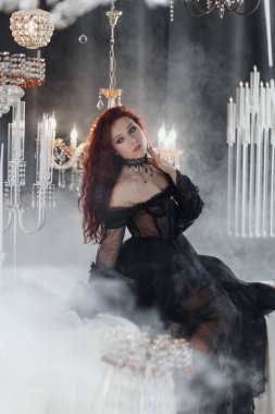 beautiful young woman with long red hair wearing black dress posing in elegant room with crystal chandeliers