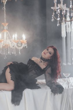 Klasik bir odada kristal avizeli siyah elbise giyen zarif kızıl saçlı kadın..