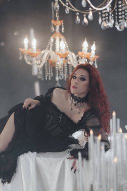 Gösterişli bir iç mekanda siyah elbiseli, göz kamaştırıcı kızıl saçlı kadın..