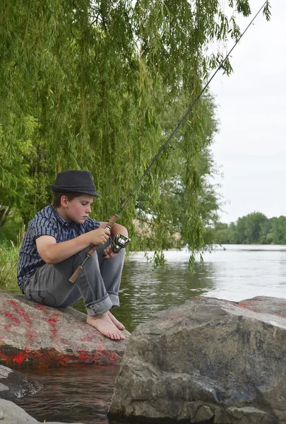 Joven pescador sentado en una roca — Foto de Stock