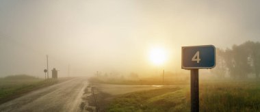 Sonbaharda sisli gündoğumunda haçta 4 numara olan mavi yol işareti..