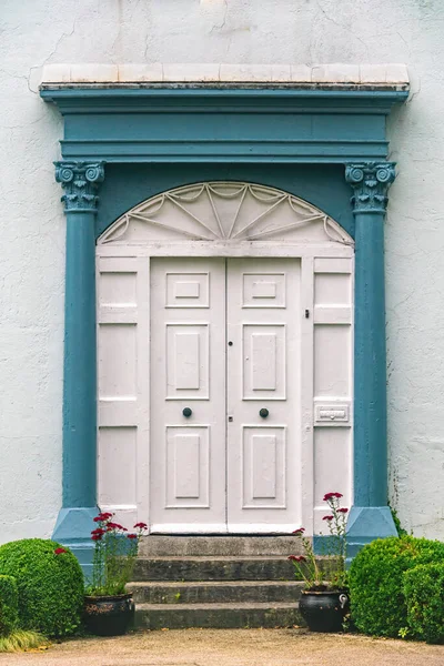 Old wooden door painted with white paint with blue columns and concrete stairs. Ireland, Cork.